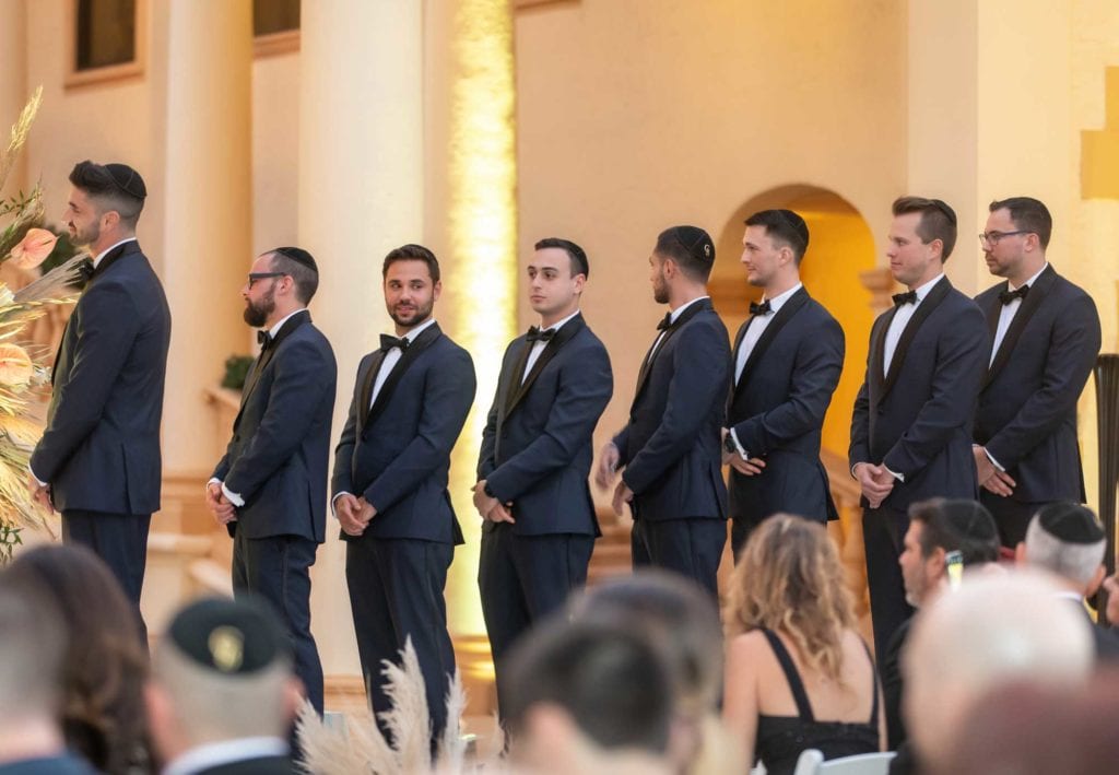 Groomsmen wearing matching black suits with bow ties stand next to groom during the ceremony at The Baltimore Hotel in Miami Coral Gables, wedding planned by Oh My Occasions