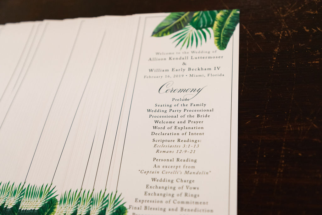 Ceremony programs decorated with monstera leaves painting laying on a table.