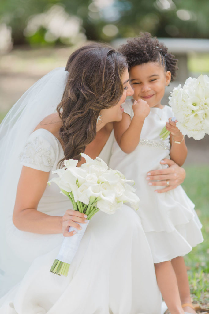 Bride laughs with the flower girl holding their white bouquets on the green lawn 