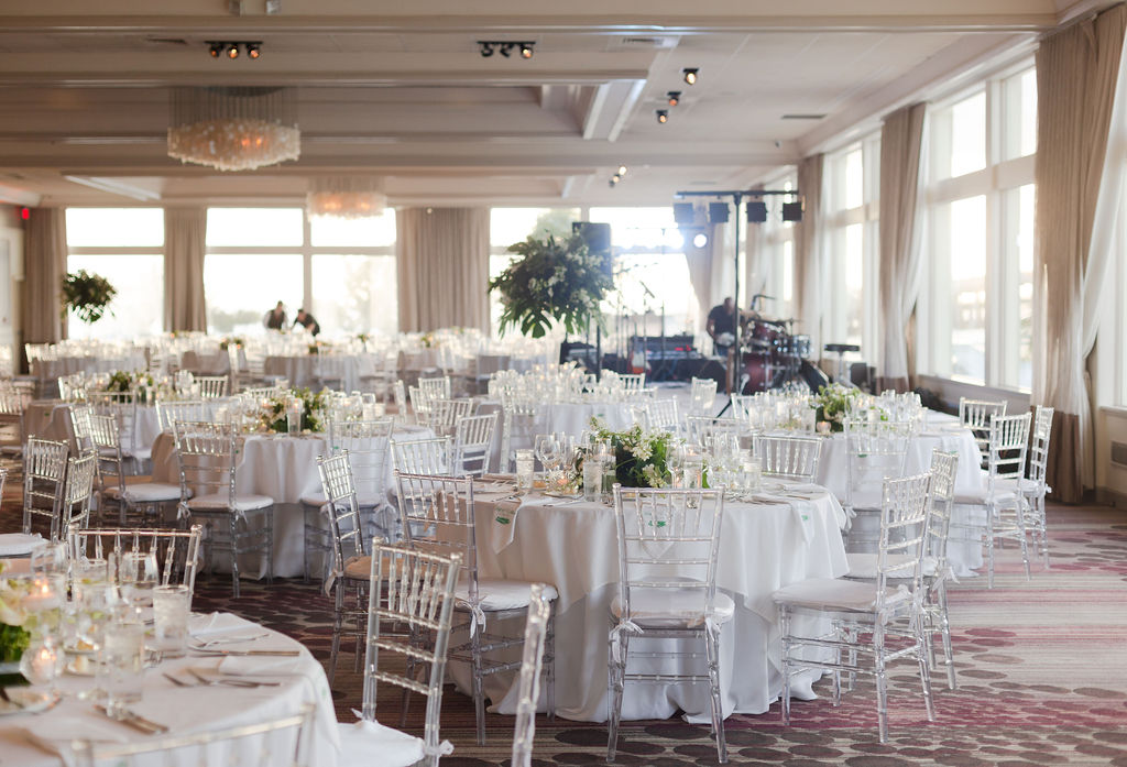 Overview of the reception area filled with round tables topped with white table linen, and green floral centerpieces at The Rusty Pelican, planned by Oh My Occasions 