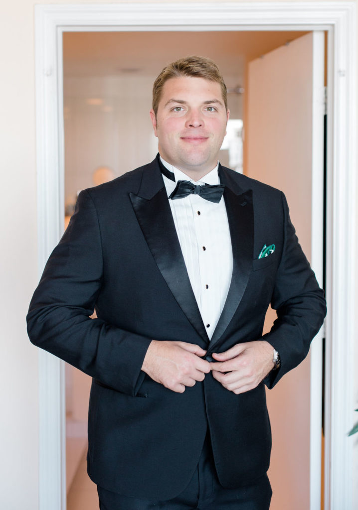 Groom smiles while buttoning his suit jacket and getting ready for the big day