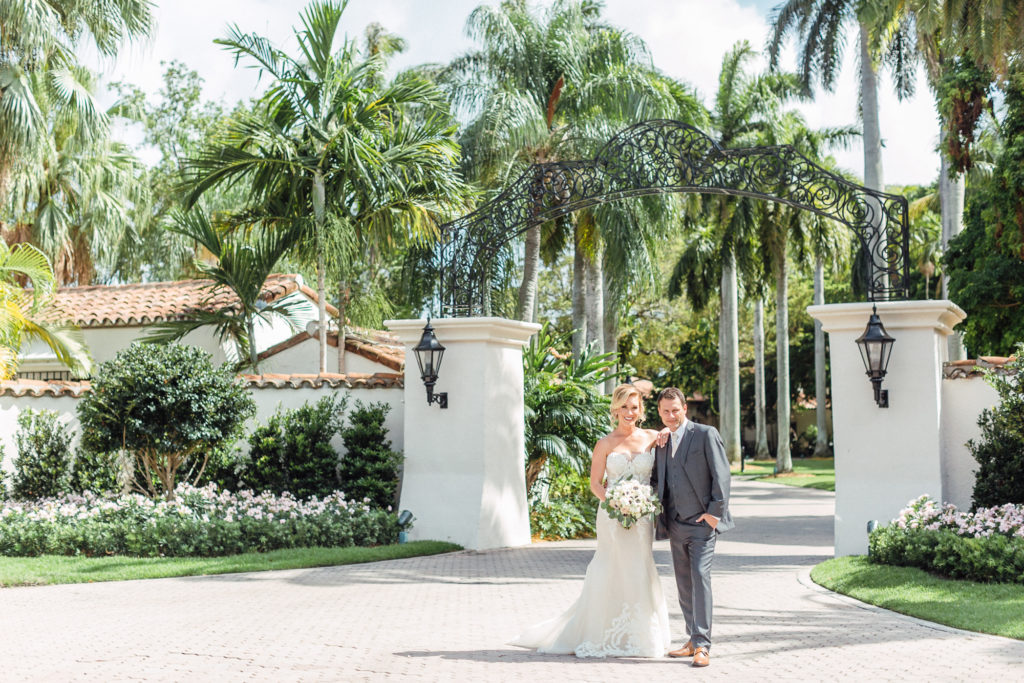 Couple stands and smiles outside gate entrance at the Fisher Island Club.