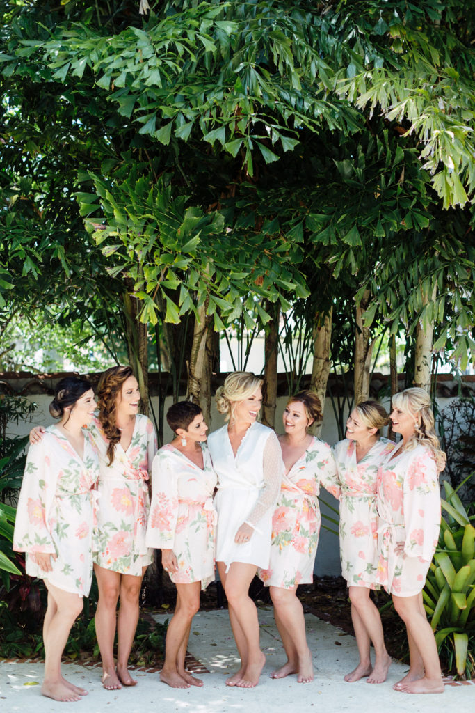 Bride stands and smiles outside with bridal party in their matching blush and floral robes.