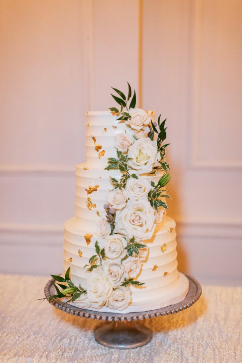 Three-tiered wedding cake with gold detailing and white flowers at The Club of Knights, wedding planned by Oh My Occasions