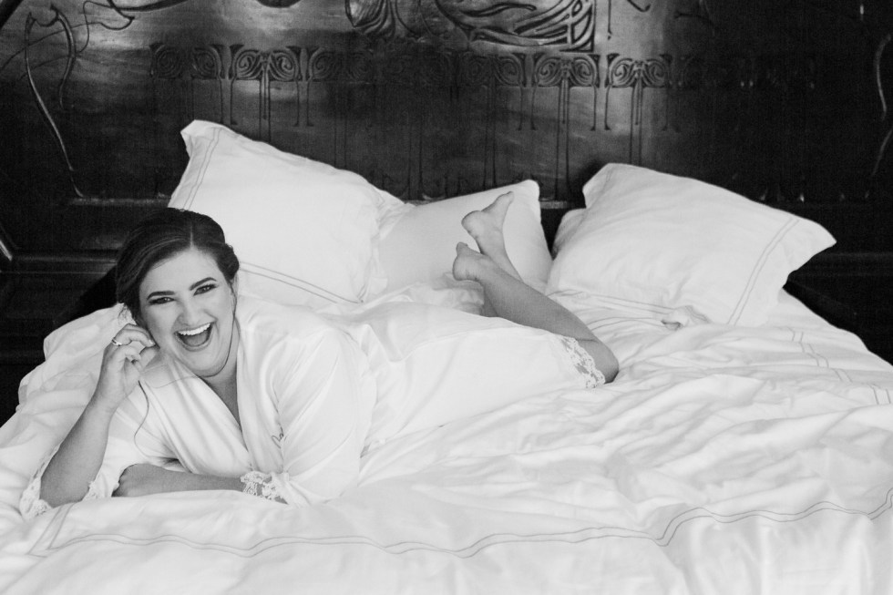 Black and white photo of bride laying on bed with her robe at The Club of Knights, wedding planned by Oh My Occasions