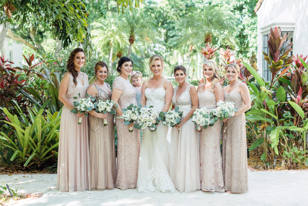 Bride stands with her bridal party wearing blush mix-matched gowns and holding their bouquets.