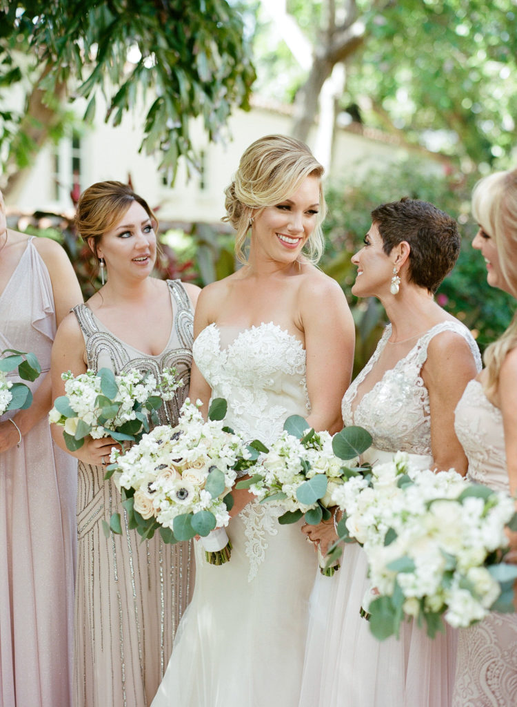 Close-up of bride standing with her bridal party looking at each other wearing blush mix-matched gowns and holding their bouquets.