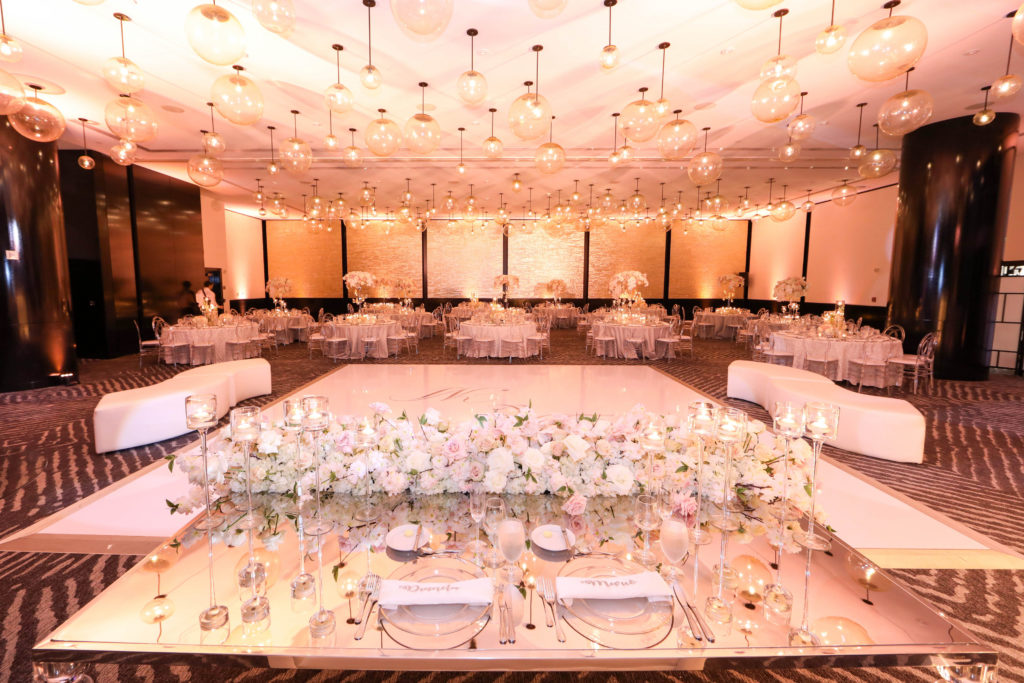 A beautiful overview of the reception ballroom with a lounge setup, wrapped dance floor, specialty sweetheart table, acrylic mirror accents, and custom love seats at the Kimpton EPIC Hotel, planned by Oh My Occasions