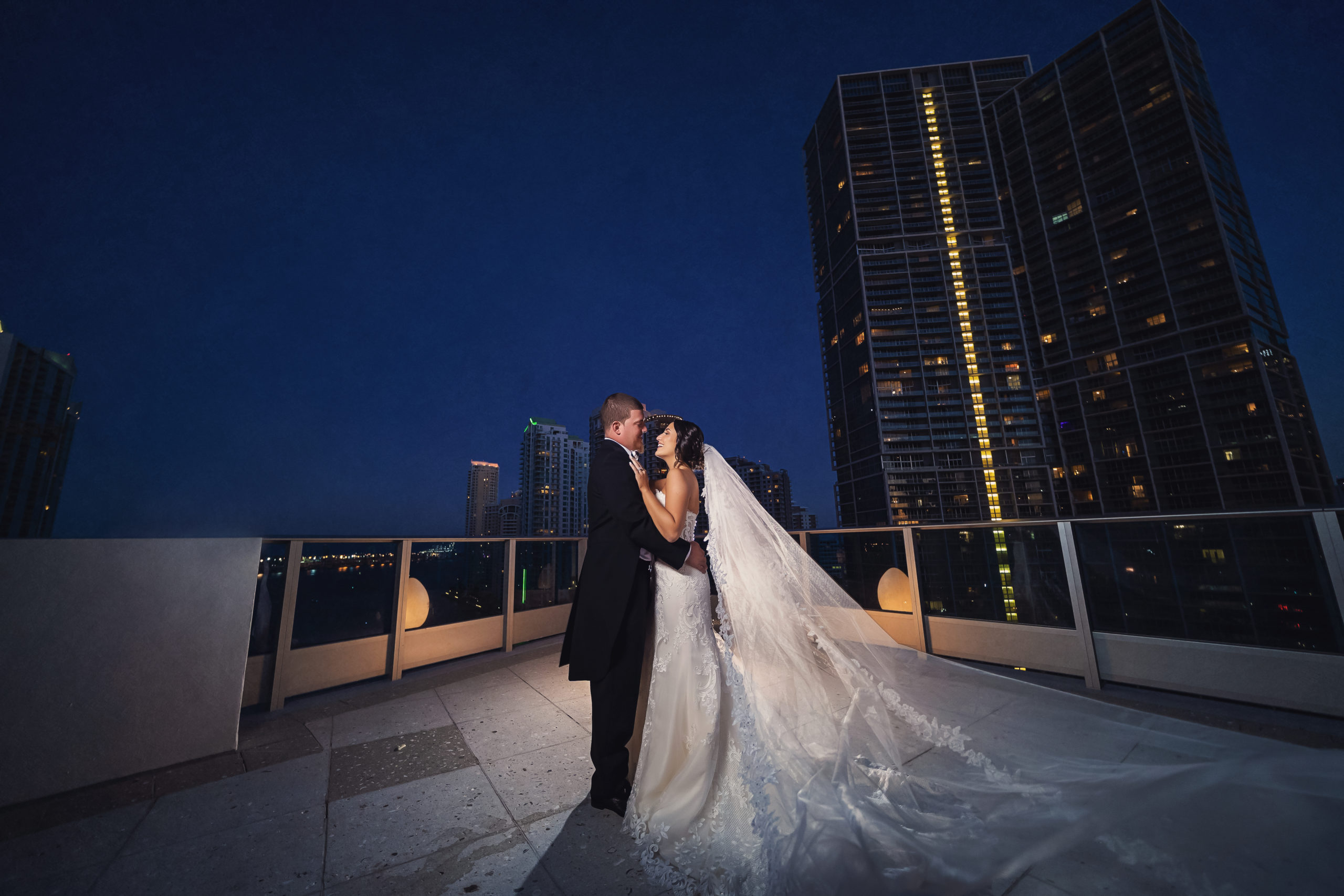 The bride and groom embracing outdoors under the dark sky on balcony at The Kimpton EPIC Hotel, wedding planned by Oh My Occasions