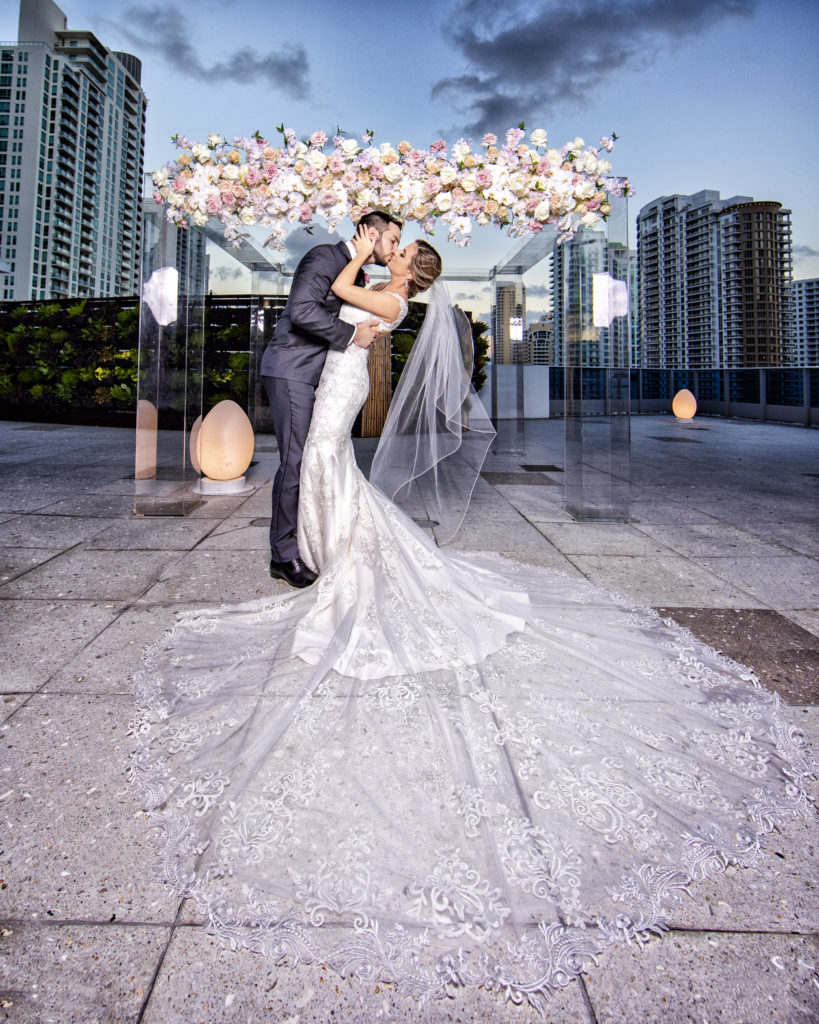 A beautiful shot of the bride and groom together in front of the custom floral acrylic structure at the Kimpton EPIC Hotel, planned by Oh My Occasions