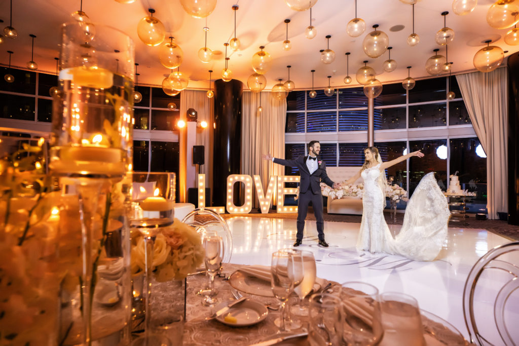 A beautiful overview of the reception venue with the bride and groom dancing on the custom wrapped floor and LOVE marquee sign in the back at the Kimpton EPIC Hotel, planned by Oh My Occasions