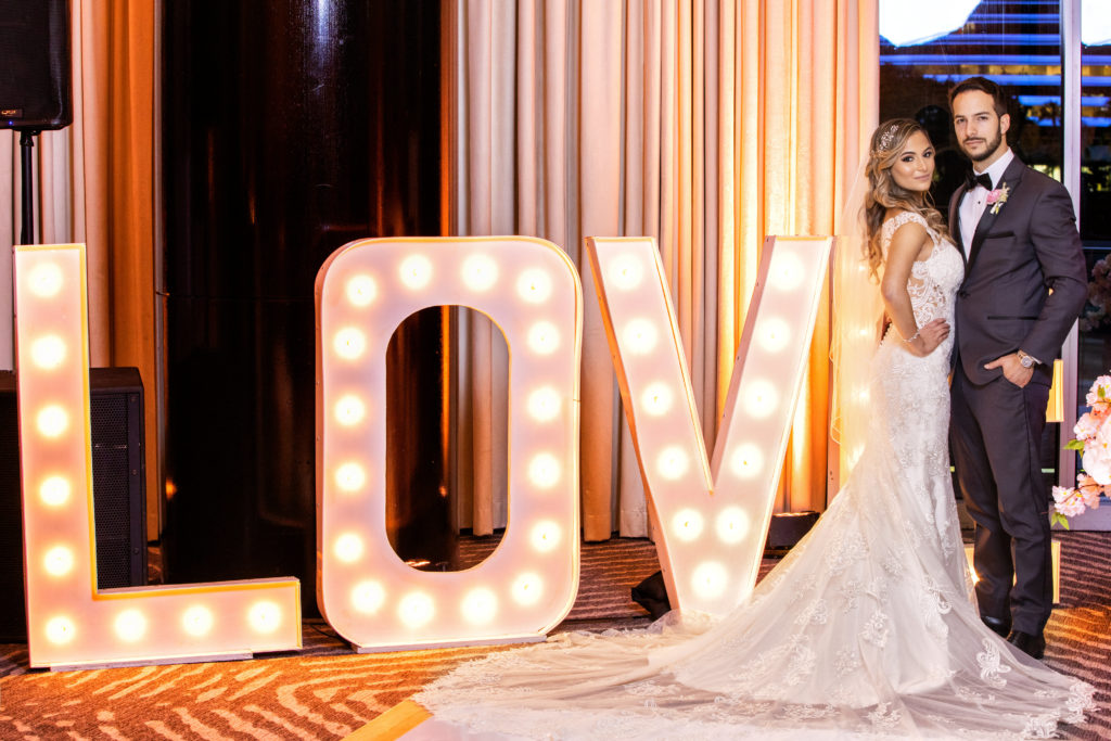 A LOVE marquee sign with the bride and groom posing at the Kimpton EPIC Hotel, planned by Oh My Occasions