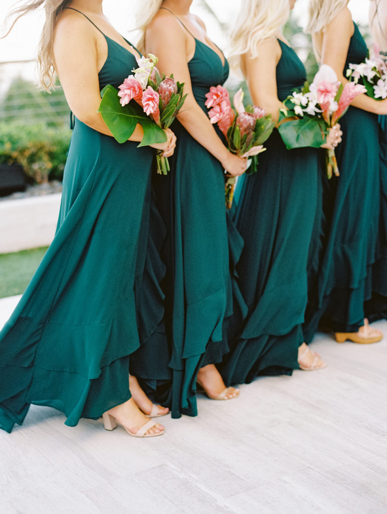 The bridesmaid's matching emerald green dresses and holding up their bouquet at Miami Beach Edition, planned by Oh My Occasions