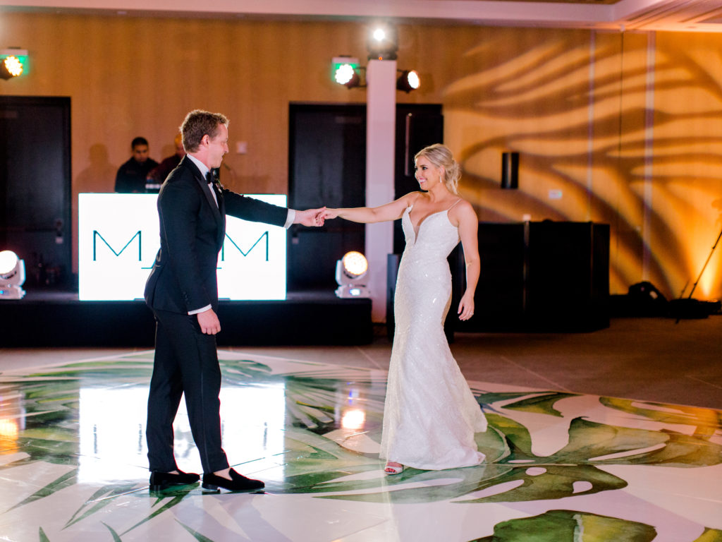 The bride and groom having their first dance on the custom wrapped tropical monstera leaf floor at Miami Beach Edition, planned by Oh My Occasions