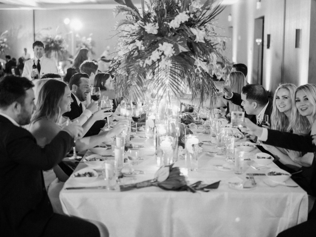 The guests at the reception dinner table holding up their drinks to celebrate at Miami Beach Edition, planned by Oh My Occasions