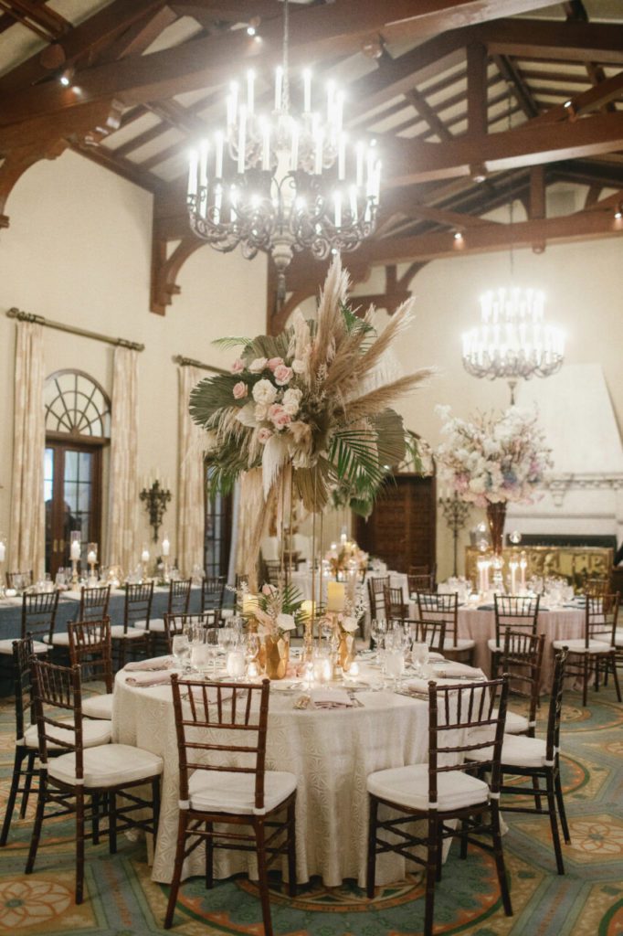 Experience a neutral dreamland at the wedding venue at Indian Creek Country Club, where pampas grass and white hanging amaranthus create a vintage, feathery setting. The addition of elegant white and light pink roses adds a touch of sophistication, while a vintage candle chandelier sets the mood for a romantic evening at Indian Creek Country Club planned by Oh My Occasions.