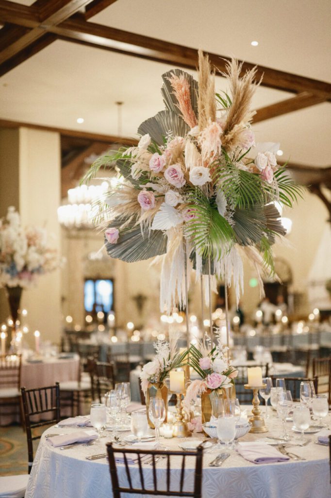 A neutral paradise at the wedding venue located in Indian Creek Country Club, where pampas grass and white hanging amaranthus create a vintage, feathery ambiance. The addition of elegant white and light pink roses adds a touch of elegance, while a vintage candle chandelier sets the mood for a romantic evening at at Indian Creek Country Club planned by Oh My Occasions.