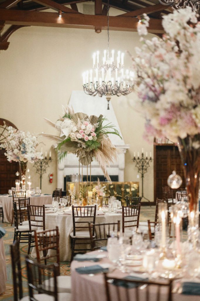 Wedding venue, where pampas grass and white hanging amaranthus create a vintage, feathery feel. The addition of elegant white and light pink roses adds a touch of sophistication, with a vintage candle chandelier at Indian Creek Country Club planned by Oh My Occasions.