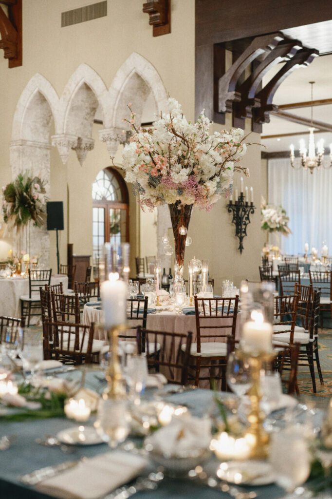 The wedding venue featuring pampas grass and white hanging amaranthus for a feathery, vintage feel. Elegant white and light pink roses add a touch of sophistication, with a vintage candle chandelier at Indian Creek Country Club planned by Oh My Occasions.