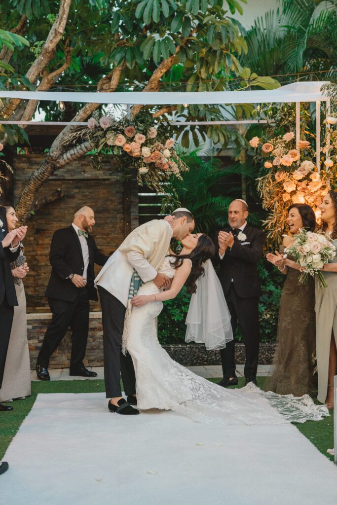 Bride and groom kiss in front of the custom chuppah at Club of Knights wedding planned and designed by Oh My Occasions