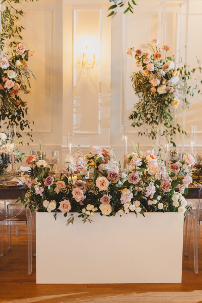 Beautiful sweethearts table adorned with pastel pink garden roses, eucalyptus, and a floral arch in the back at Club of Knights wedding planned and designed by Oh My Occasions