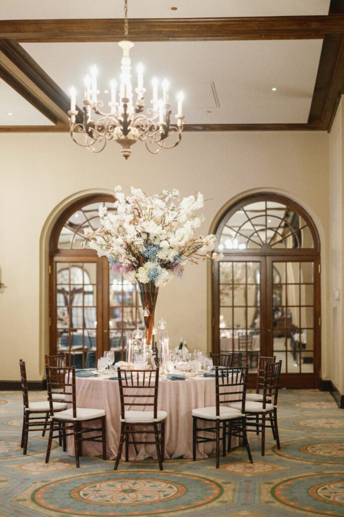 The floral centerpiece is arranged beautifully with mahogany branches with muted blush and dusty blue florals. It ties the entire venue and theme wonderfully together at Indian Creek Country Club planned by Oh My Occasions.