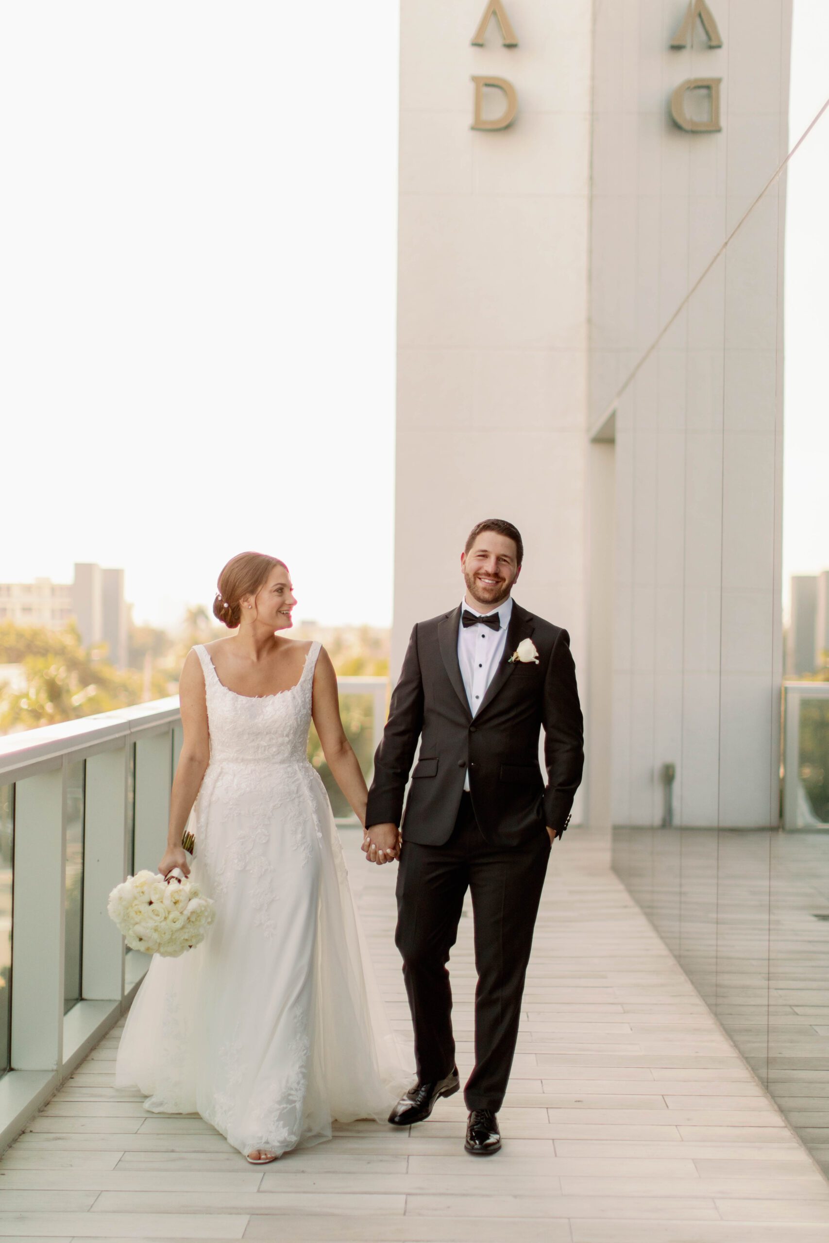 The bride and groom holding hands outside on the balcony and walking towards the camera at The Conrad Hotel, wedding planned by Oh My Occasions