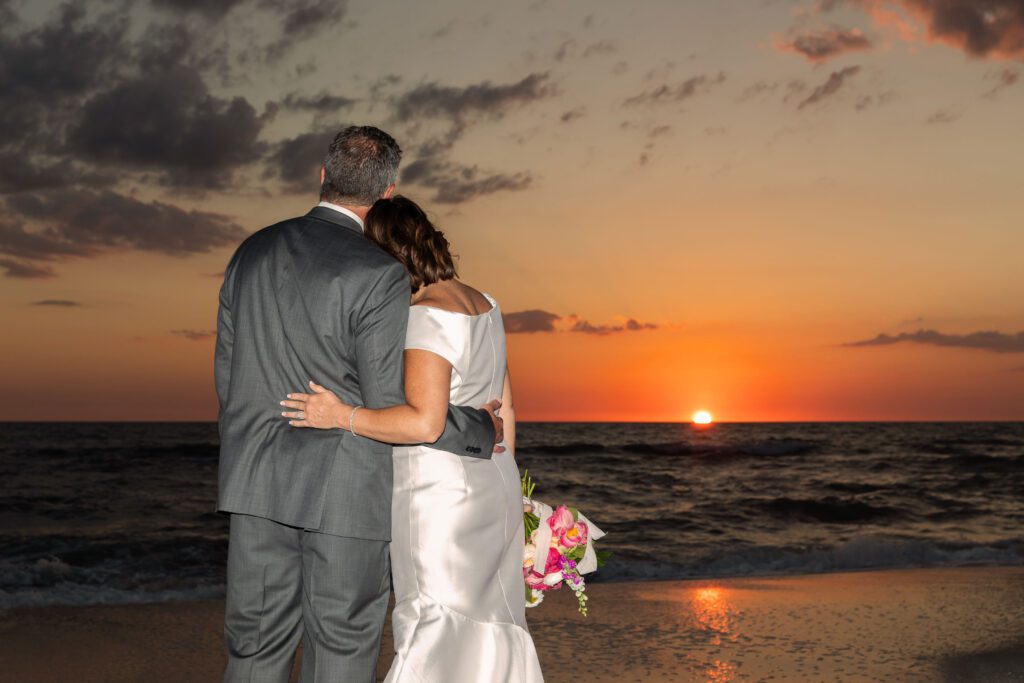 a bride and groom look out as the sun sets on the ocean at La Playa Golf and Beach Resort in Naples Florida
