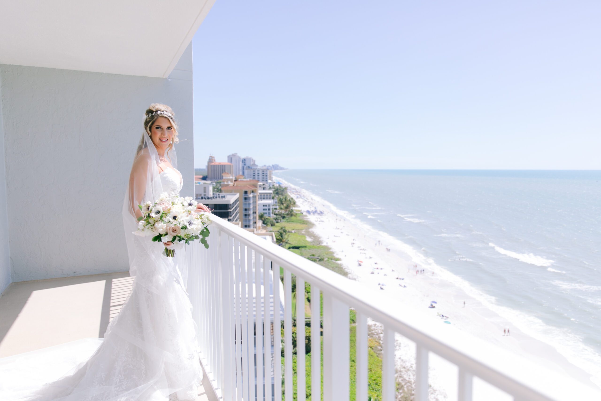 a bride stands on her balcony overlooking the ocean at La Playa Golf and Beach Resort in Naples Florida